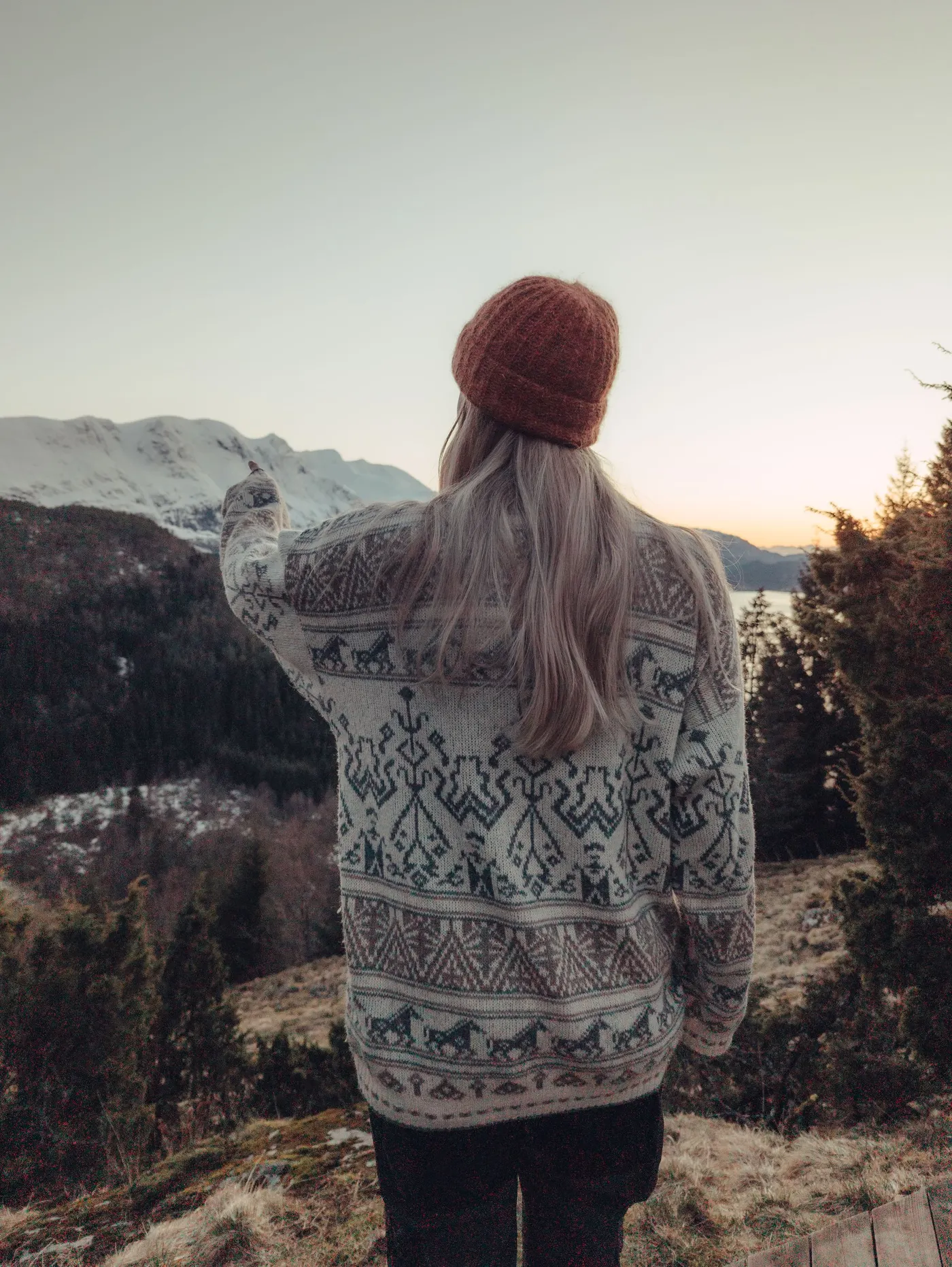 Person in a patterned wool sweater watching sunset over mountains